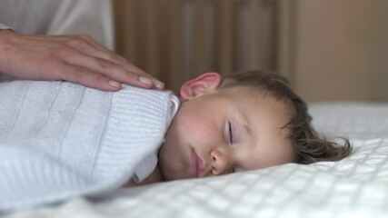 Poster - Authentic close up of mother is kissing her toddler baby boy while sleeping by day in crib with soft blanket in a nursery. Concept of family, comfort,care, love, sweet dreams, motherhood, childhood.