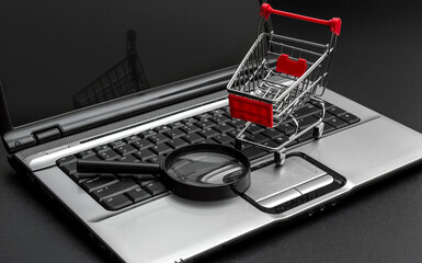 Shopping cart with magnifying glass and laptop on black background. Find purchase online.