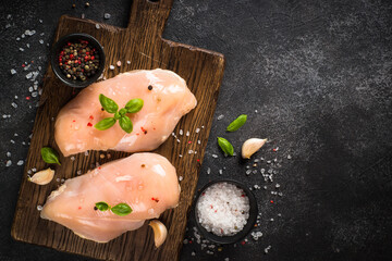 Chicken fillet with spices and herbs at black table.