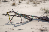 Plastikowe przedmioty zawieszone na suchym konarze leżącym na plaży.