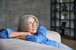 © insta_photos - Mature peaceful 60s middle age lady sitting relaxing at home. Senior elder serene woman in glasses looking at window thinking of positive vision, dreaming of future and enjoying wellbeing.
