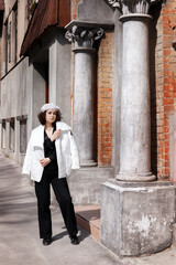 girl in a white beret and white jacket near an old building