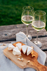 Two glasses of white wine and a wooden plate with cheese and nuts served outside at sunset.