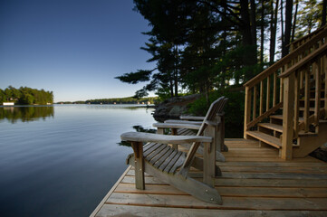 Two Adirondack chairs on a wooden dock facing a lake in Muskoka, Ontario Canada early summer morning. Retirement aspirations and financial planning concept