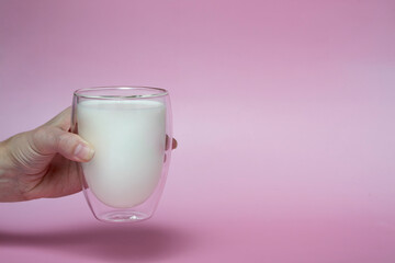 female hand holding a glass with fresh milk, on a pink background,fortified drink, calcium