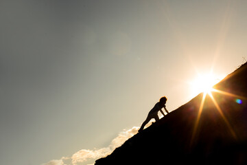 Man climbing a mountain with the sun in the background. Concept of never give up on your goals and dreams