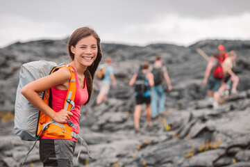 Wall Mural - Hawaii volcano hike adventure happy Asian woman with backpack in Big Island, Hawaii. Hiking group of tourists walking on black lava field trail. Smiling Asian girl outdoor USA summer travel vacation.