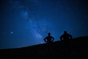 Poster - Magical view of silhouettes of two men stargazing, admiring the Milky way and the blue night sky