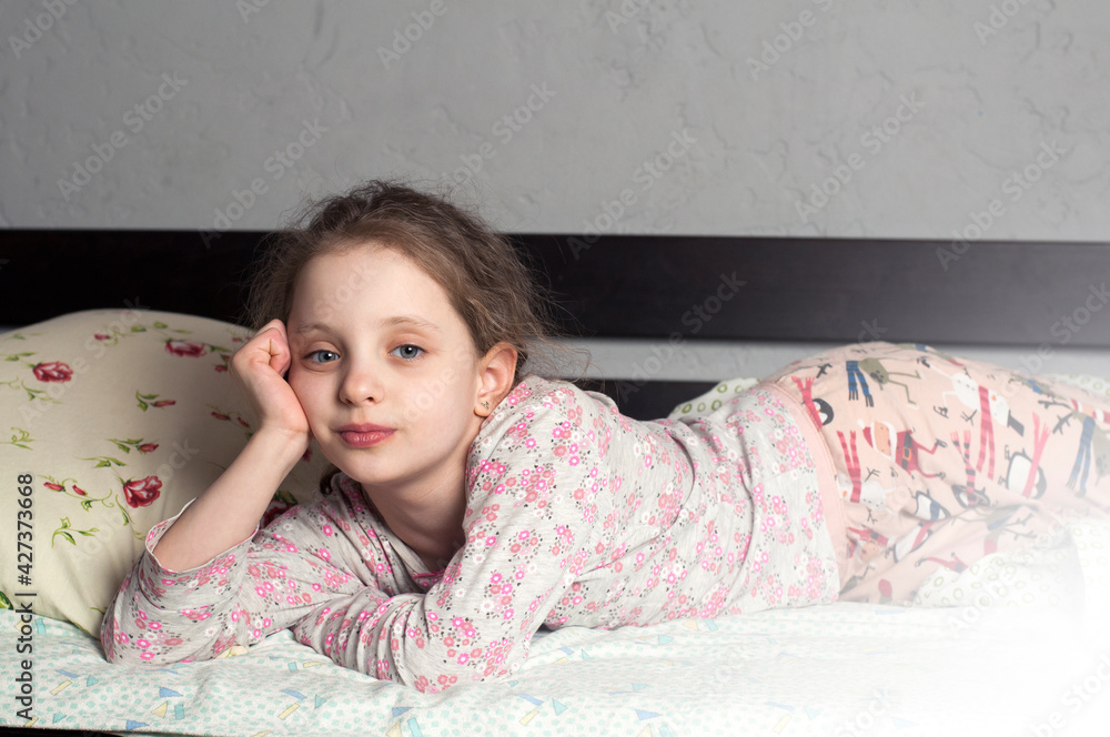 The girl is a European 10 years old. Lies in his pajamas on the bed. In the bedroom. Stock Photo Adobe Stock
