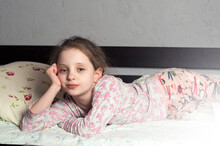 The Girl Is A European 10 Years Old. Lies In His Pajamas On The Bed. In The Bedroom.