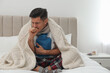 © New Africa - Ill man with hot water bottle coughing at home