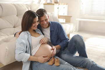 Wall Mural - Young pregnant woman and her husband with baby's shoes at home