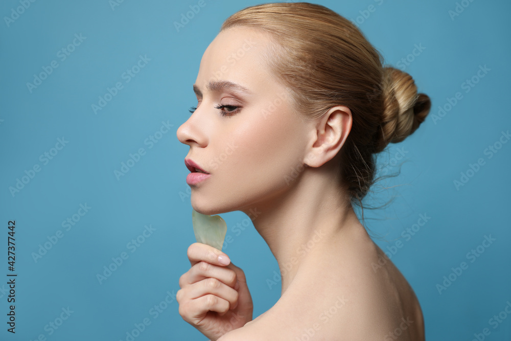 Beautiful young woman doing facial massage with gua sha tool on blue background, closeup - obrazy, fototapety, plakaty 