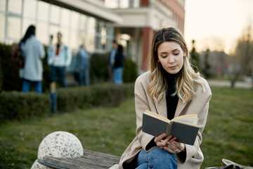 Wall Mural - Female university student reading book while relaxing outdoors at campus.