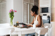 © Drobot Dean - Black woman working with papers while sitting at table in home kitchen