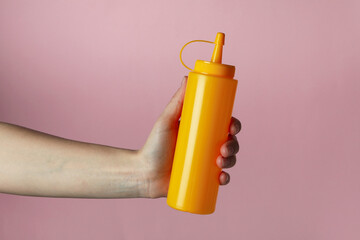 Female hand hold yellow sauce bottle on pink background