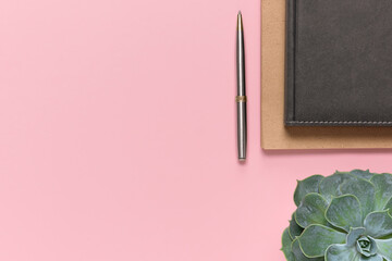 Notepads, a pen and a home flower on a pastel pink background with space for text. Home office workspace. Flat lay