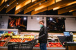© Dragica - A young caucasian  man with a face mask pushes a basket in the supermarket and buys fruit. Procurement of food during the coronavirus pandemic crisis
