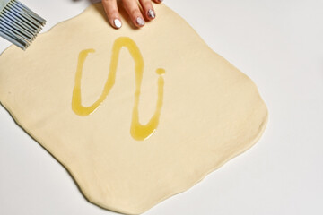 Sticker - Person spreading olive oil on yeast dough for making a pie on a white surface