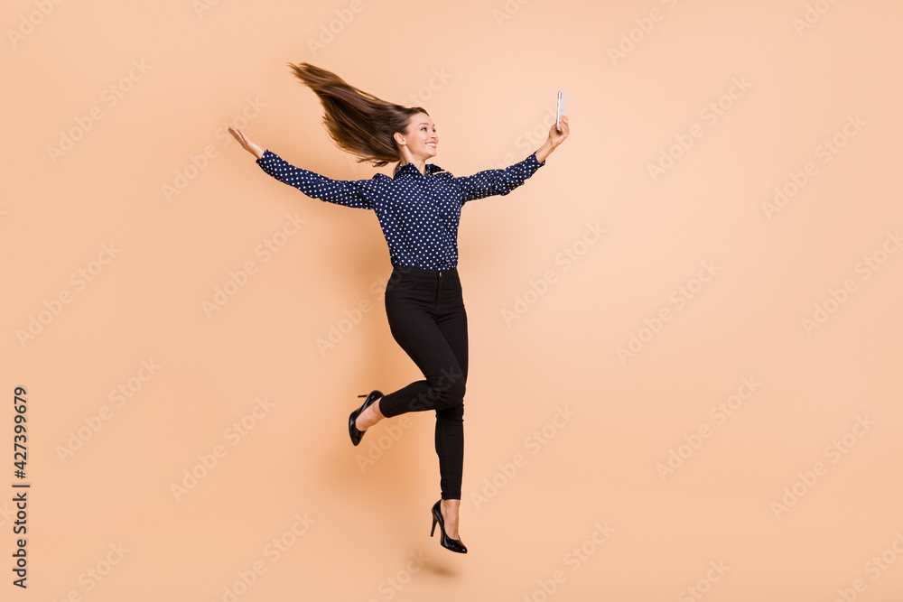Full length profile side photo of young woman happy smile jump up make selfie cellphone isolated over beige color background - obrazy, fototapety, plakaty 