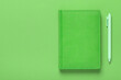 Green notebook with a pen on a green background with copy space. Abstract background in a simple business style.