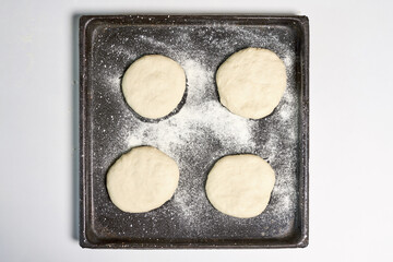 Sticker - Top view of four pieces of dough in a black pan with flour