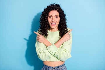 Wall Mural - Photo of excited young lady indicate fingers two directions empty space wear green pullover isolated blue background