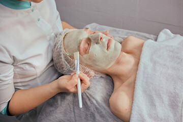 There is green clay on the man's face. Professional facial skin care. Applying clay to the face with a brush.