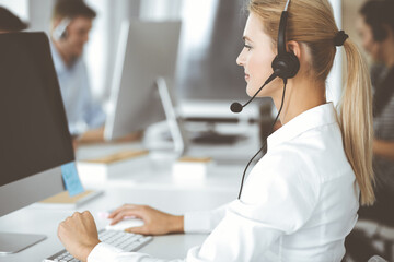 Blonde business woman using headset for communication and consulting people at customer service office. Call center. Group of operators at work