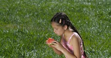 Profile Portrait Of Cute Little Girl Of  Eight Years Old Sitting On The Lawn And Eating Watermelon Slice . Concept Of Organic Fruits And Healthy Vegetarian Diet.  50 Fps Slow Motion