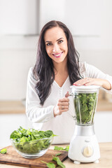 Wall Mural - Good looking girl ina home kitchen preparing healthy raw food in a form of green smoothie