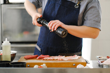 Wall Mural - The chef salts and peppers a piece of meat. Cooking in the kitchen of restaurant.