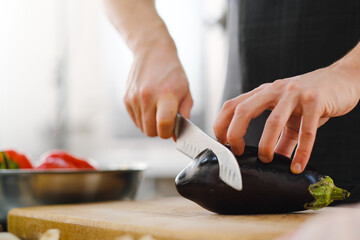 Wall Mural - The male Caucasian chef cuts vegetables, peppers, tomatoes and eggplants on a wooden cutting board.