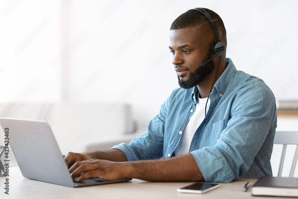 Black millennial man in headset working remotely with laptop at home office - obrazy, fototapety, plakaty 