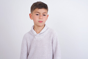 Caucasian kid boy wearing knitted sweater against white wall looking sleepy and tired, exhausted for fatigue and hangover, lazy eyes in the morning.