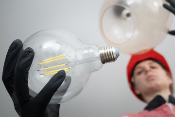 electrician in uniform and hard hat changing large vintage style light bulb in pendant lamp indoors	