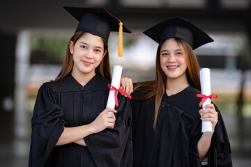 Wall Mural - Young happy Asian woman university graduates in graduation gown and mortarboard hold a degree certificate celebrate education achievement in the university campus.  Education stock photo