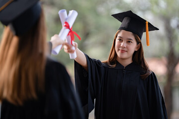 Wall Mural - Young happy Asian woman university graduates in graduation gown and mortarboard hold a degree certificate celebrate education achievement in the university campus.  Education stock photo