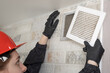 A professional worker in a protective suit and helmet cleans the Ventilation grill. Flat Panel Fiberglass Filters Of Central Air Condition System With Dust.	
