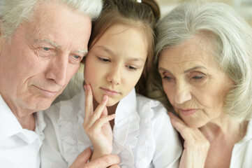 portrait of sad grandmother, grandfather  and granddaughter hugging at home