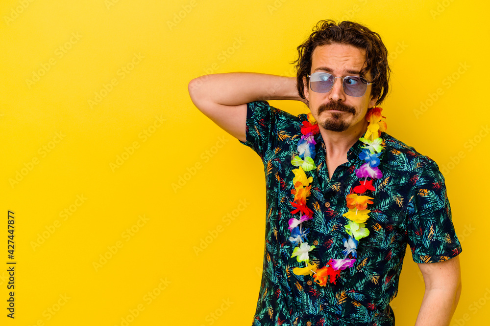Young caucasian man wearing a hawaiian necklace isolated on yellow background touching back of head, thinking and making a choice. - obrazy, fototapety, plakaty 