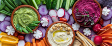 Narrow Close Up View Of Three Dips Surrounded By Fresh Cut Vegetables For Dipping.