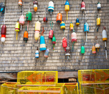 Lobster Buoys Hanging On The Wall Of A Building With Yellow Lobster Pots On The Ground