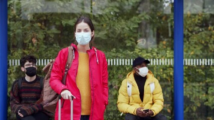 Wall Mural - Young people waiting for bus at bus stop, looking at camera. Coronavirus and safe distance concept.