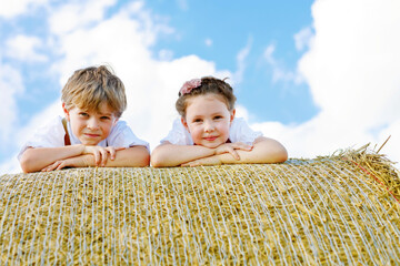 Wall Mural - Closeup of two kids laying on hay bale in wheat field. Portrait of german children during Oktoberfest. Preschool Boy and girl play at hay bales during summer harvest time in Germany.