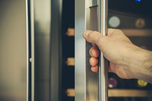 A Hand Opens The Door Of The Wine Refrigerator