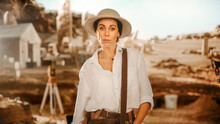 Portrait Of Beautiful Female Adventurer Posing And Looking At Camera. Stylish Great Archaeologist Standing With Ancient Civilization, Fossil Remains Archeological Site, Forgotten City In Background