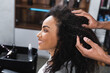 Side view of smiling african american client sitting near hairstylist touching hair