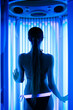 Young sexy female in a tanning cabin of vertical solarium. girl sunbathing in solarium cabin with blue luminous tanning lamps in bikini