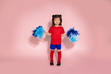 Young Girl As Cheerleader Standing On Pink Background, Kid With Blue Pom Poms